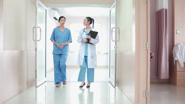 Professional, Team Multiethnic Medical Group. Asian Female Doctor And Nurse, Staff Walking In Hospital Corridor. Colleague Hospital  Workers Greet, Discussing, Report With Clipboard In Clinic Hallway.