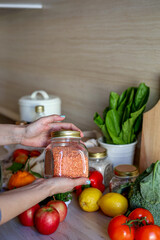 Young Asian woman takes out a glass jar of lentils from a grocery bag. Reusable package. Zero waste.