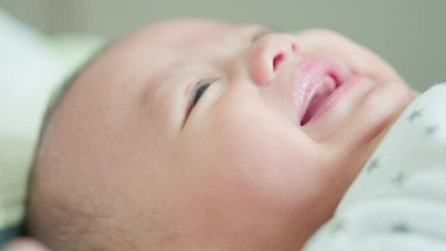 Close-up of face cute asian newborn baby lying play on white bed look at camera with laughing smile happy face. Innocent little new infant adorable. Parenthood and Mother Day concept.