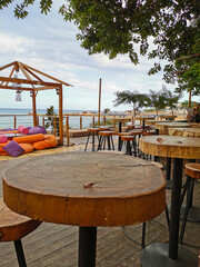 Cafe next to the beach. Tables and bar stools made from sawn wood, a tent with soft, low mattresses, scattered multi-colored pillows and decorative lanterns