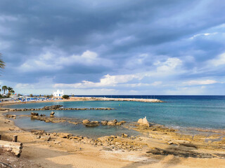 Rocky shore with sand, sandy beach, the temple of St. Nicholas the Wonderworker against the backdrop of a dramatic sky.