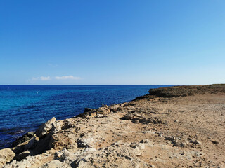 View from the rocky shore to the blue sea to the horizon against a blue sky with clouds.