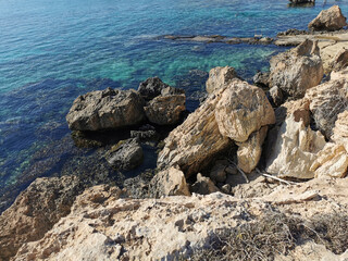 Rocky coast of the Mediterranean Sea with large stones, clear water through which the bottom is visible.