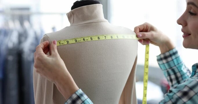 Seamstress takes measurements from clothes on mannequin