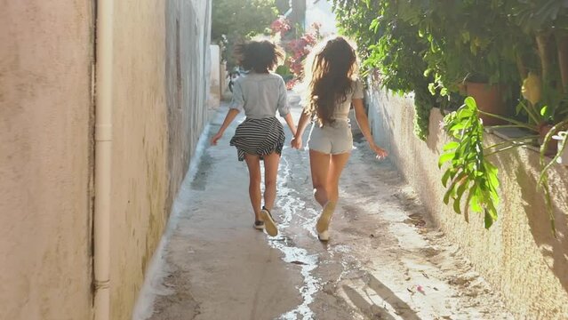 Two girls running across sunny greek street. Best friends spend summer time together and girls enjoy life. woman road by car to sea. Friendship and love forever, Concept of Lifesyle people, travel and