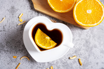 Fruit hot tea with orange in a heart cup and fresh oranges on a gray table