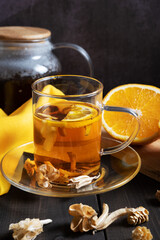 A glass cup of orange fruit tea in the foreground on a dark wooden table
