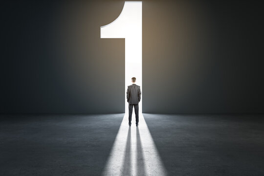 Way to success and leadership concept with back view on businessman looking at sunlight from number one entry in empty dark hall
