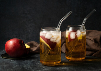 Two glasses of apple juice cocktail with ice on a dark background