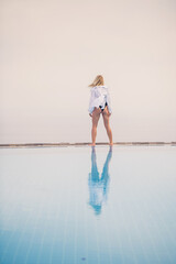 An attractive young woman in a black swimsuit and white shirt stands near the pool with a panoramic view.