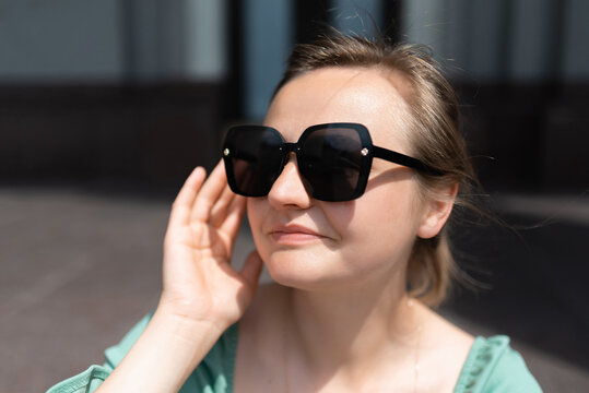 Attractive young woman touching sunglasses and smiling