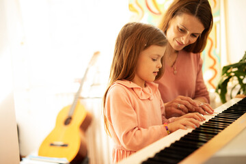 Woman and girl playing a piano. Beautiful mom teaching her daughter playing a piano..