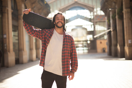 Portrait of young handsome guy with skateboard. Happy smiling skater using the phone.