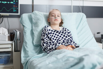 Lonely young pale sick girl patient resting in pediatric clinic bed while in recovery ward room....