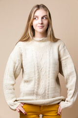 Happy Smiling Winsome Caucasian Blond Female Wearing Knitter Decorated Warm Sweater while Looking to Side Over Beige Background.