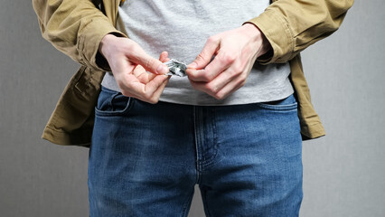 Man puts hands into jeans pockets looking for money. Male person finds stash taking out crumpled...