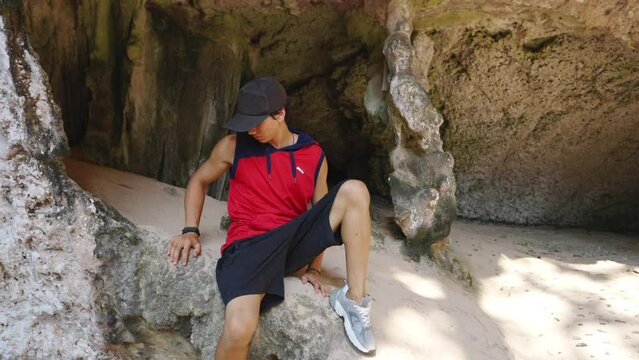 Young Asian man solo travel in rock mountain cave on tropical island beach lagoon in summer sunny day. Happy guy relax and enjoy outdoor activity lifestyle on summer holiday vacation trip in Thailand