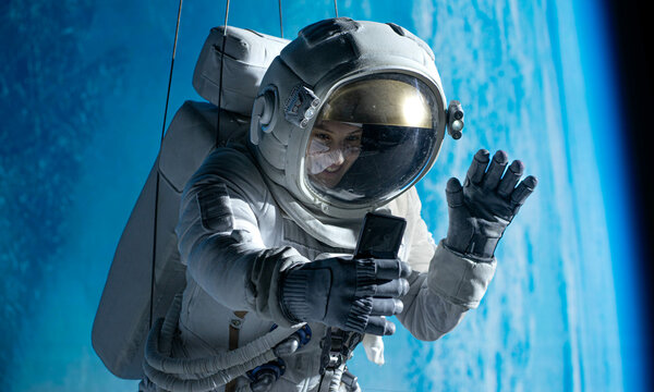 Behind the scenes of commercial shot - Caucasian female astronaut stuntwoman hanging on a wires, wearing a spacesuit