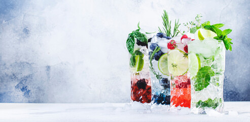Summer cocktails or mocktails and cold drinks. Refreshing mojito drink with blueberries, blackberries, raspberries and  lime, herbs and ice on gray background