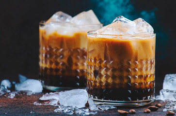 Trendy alcoholic cocktail drink with vodka, coffee liqueur, cream and ice on dark background, ...