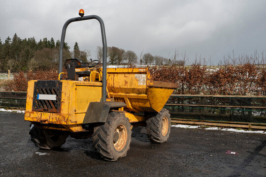 Old rusty dumper track parked on a parking lot in a country side. The vehicle is yellow color has many scratches. Warm sunny day. Cloudy sky. Construction and repair equipment for rent concept.