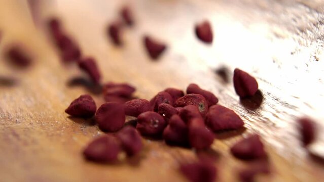 Achiote seeds. Annatto grains falling on a wooden surface of rustic bowl. Red natural culinary dye for cooking. Mexican seasoning. Macro. Slow motion