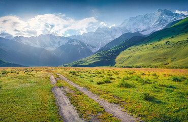 Old country road in Caucasus mountains. Majestic summer view of Shkhara peak, Ushguli location, Georgia, Europe. Splendid outdoors scene of Upper Svaneti. Traveling concept background..