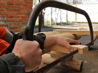 sawing off the edge of a bar in the structure of a wooden structure with an arc saw in a rural yard, a hand saw in the process of woodworking in a village, hacksaw work in a village yard - obrazy, fototapety, plakaty