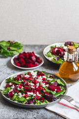 Arugula, Beet and cheese salad with pomegranate and dressing on plate on grey stone kitchen table background, place for text, top view