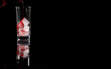 Pouring red non alcoholic solution on the top of the ice into the glass against complete dark background. copy space.