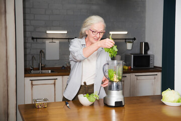 Healthy nutrition in the family, vegetarianism. Senior lifestyle. elderly woman makes smoothie from greenery and superfoods in the kitchen at home