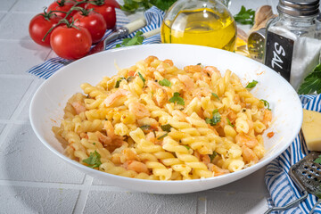 Italian mediterranean lunch concept. Fusilli pasta with seafood, shrimp, vegetables and creamy sauce. On a white tile table, with spices for dinner copy space