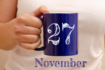 The inscription on the blue cup 27 november. Cup in female hand, business concept