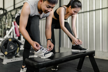 exercise concept The man and woman in the sport club resting one of their feet on the black bench and trying to tie up their shoelace