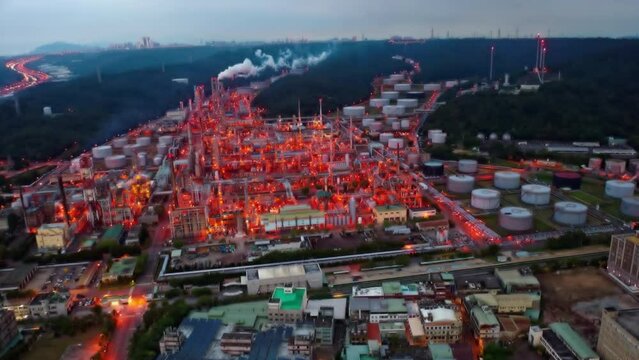 Aerial hyperlapse over a CPC oil refinery plant in a petrochemical industrial estate, with huge storage tanks and pipelines throughout the factory and the lights glowing at dusk in Taoyuan, Taiwan