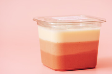 Three layers of different types of bird's milk in plastic packaging against pink background.