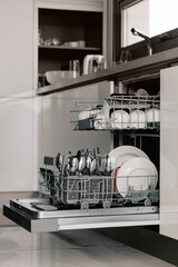 Clean dishes in dishwasher. Set of white plates, mugs and spoons in modern kitchen.