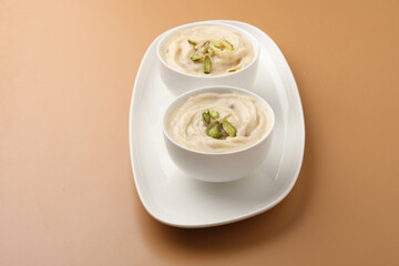 Shrikhand is an Indian sweet dish made of strained curd,garnished with dry fruits and saffron. Served in a ceramic bowl.Selective focus