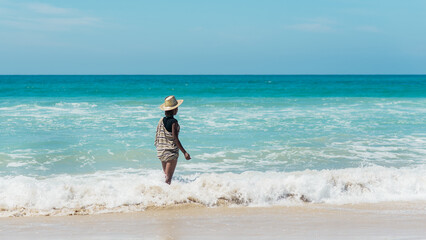 Junge Frau mit Hut in den Wellen im t&uuml;rkisfarbenen Meer in S&uuml;dafrika horizontal