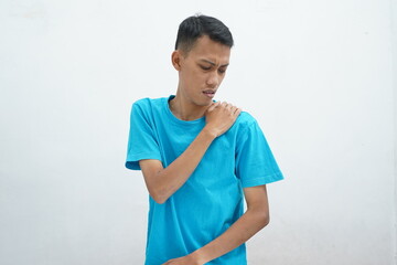 Asian young man wearing blue t-shirt suffering from shoulder pain from trying, isolated on white background