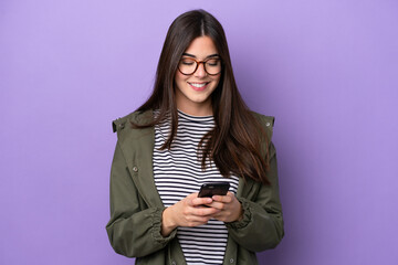 Young Brazilian woman isolated on purple background sending a message with the mobile