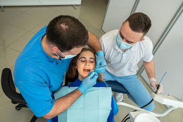 Obraz premium Dentist and assistant in mask treats teeth female patient at the dental office