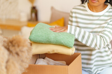 Faceless ethnic female putting clothes in box. Concept of moving house and packing stuff