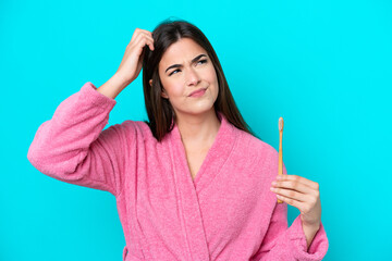 Young Brazilian woman brushing teeth isolated on blue background having doubts and with confuse face expression