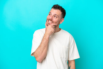 Young Brazilian man isolated on blue background looking up while smiling