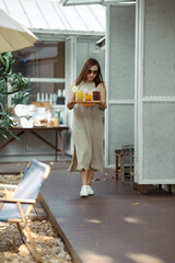 Asian women in long dresses serve coffee and fruit juice in the cafe shop. Female walking and holding a tray of coffee. Self-service in a coffee shop