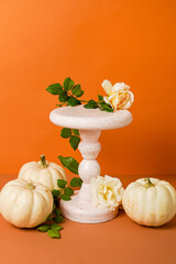 Halloween background podium display with pumpkins and flowers on orange background. Cosmetic,...