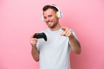Fototapeta na wymiar Young Brazilian man playing with video game controller isolated on pink background pointing front with happy expression