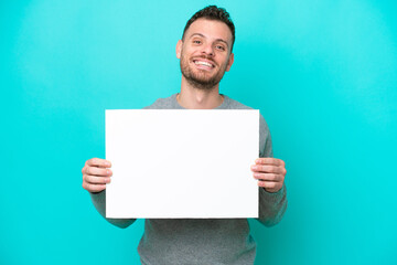 Young Brazilian man holding an empty placard isolated on blue background holding an empty placard with happy expression