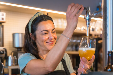 Smiling waitress brewing a blonde beer in a tap, covid restrictions are lifted and the mandatory...